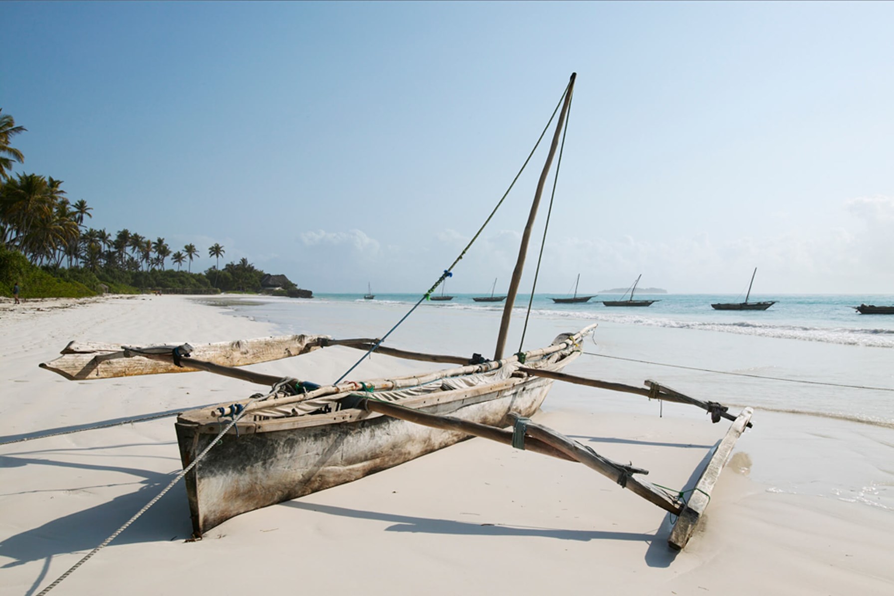Dhow boat on the beach with sea in front of it and other dhow boats off the coast of Zanzibar