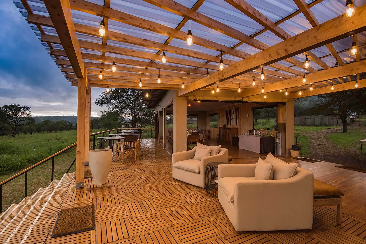 Wooden deck and with strings of bulbs hanging from the rafting with couches looking over the Serengeti