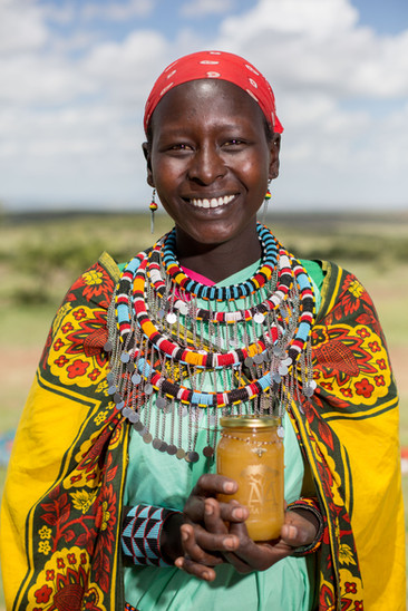A smiling Maasai lady proudly displays a bottle of Maa Trust honey.