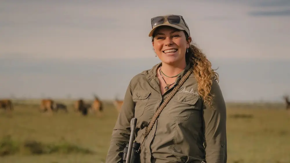 Menina stand against a backdrop of sprawling plains and smiles warmly at the camera