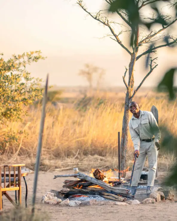 Chairs placed around a campfire where a waiter is tending the flames