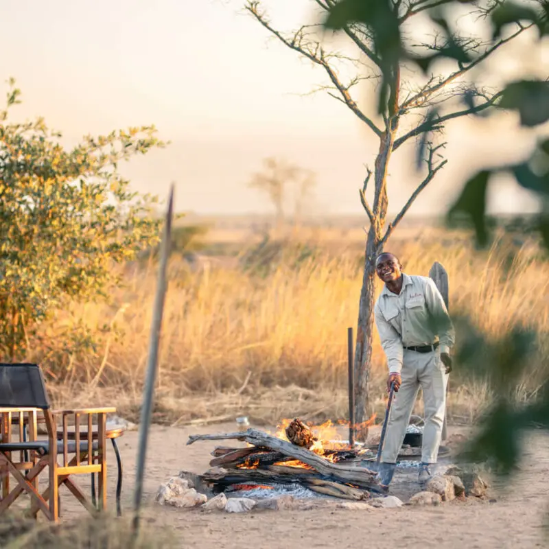 Chairs placed around a campfire where a waiter is tending the flames