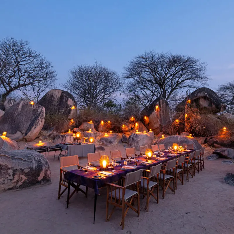 A luxurious dinner set up in the outdoors, surrounded by boulders
