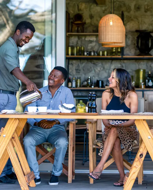 Three guests sit at a table where a waiter pours their drink