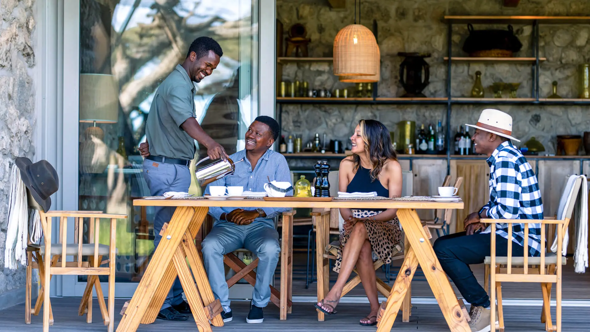 Three guests sit at a table where a waiter pours their drink