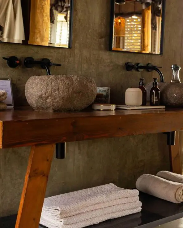 Jabali Private House bathroom with a wooden vanity, stone basin sinks, neatly folded towels, and natural light filtering through shuttered windows.