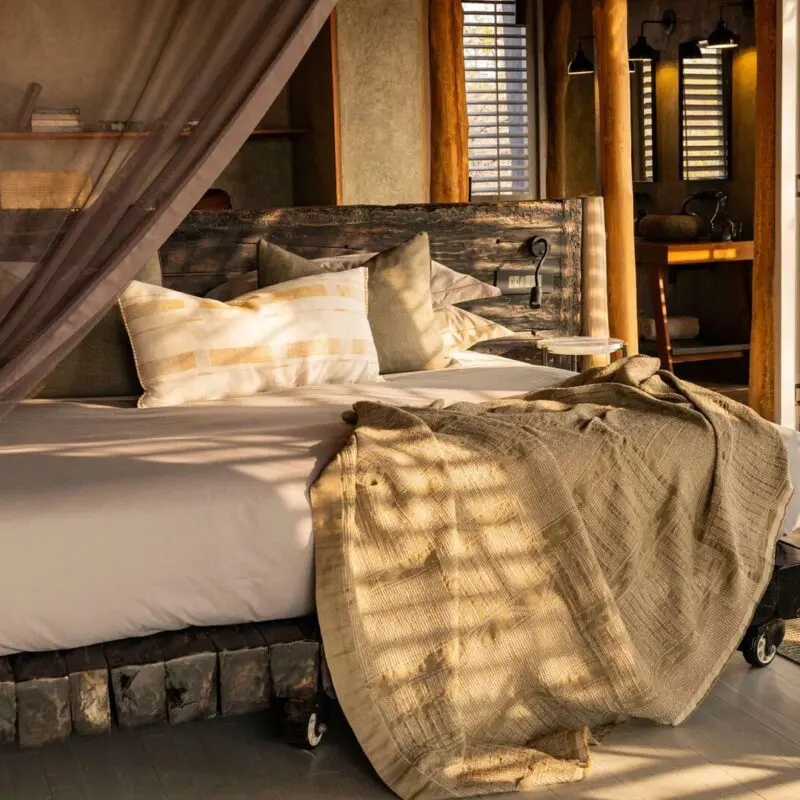 Jabali Private House, bedroom with a large bed draped in neutral linens and a mosquito net, wooden furnishings, and open shutters letting in warm natural light.