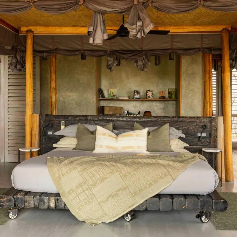 Jabali Private House - spacious safari lodge double bedroom with a four-poster bed draped in soft linens, wooden pillars, open shutters, and natural light flowing through the room.