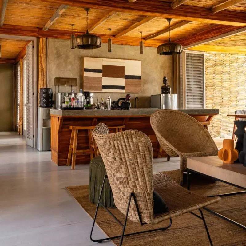 Jabali Private House lounge with woven chairs, a wooden bar, open shutters, and natural light filtering through, set within a safari lodge environment.