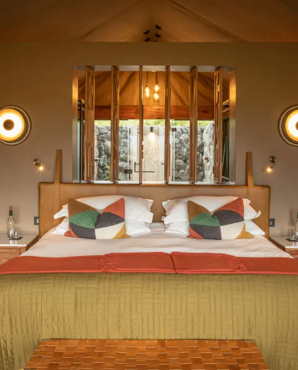 A bedroom at Naboisho Camp with a large bed, patterned cushions, and soft lighting on either side