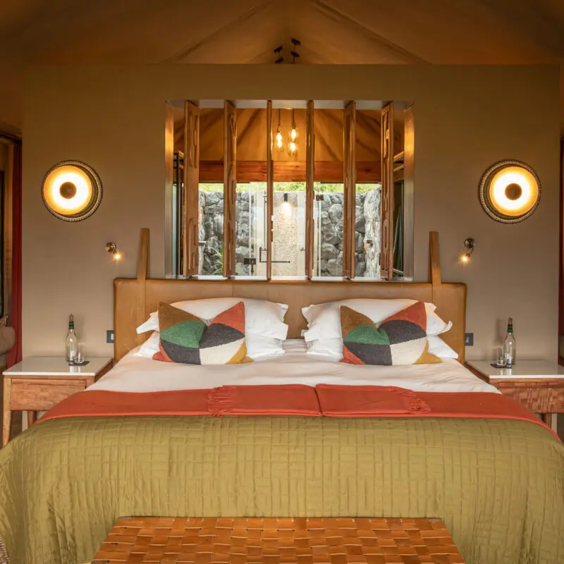 A bedroom at Naboisho Camp with a large bed, patterned cushions, and soft lighting on either side