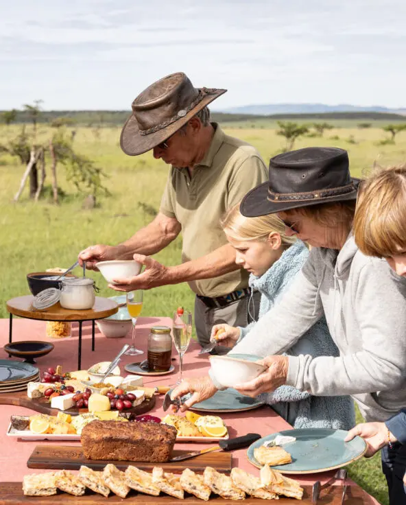Guests and children serving themselves food at a bush breakfast table set in open grassland
