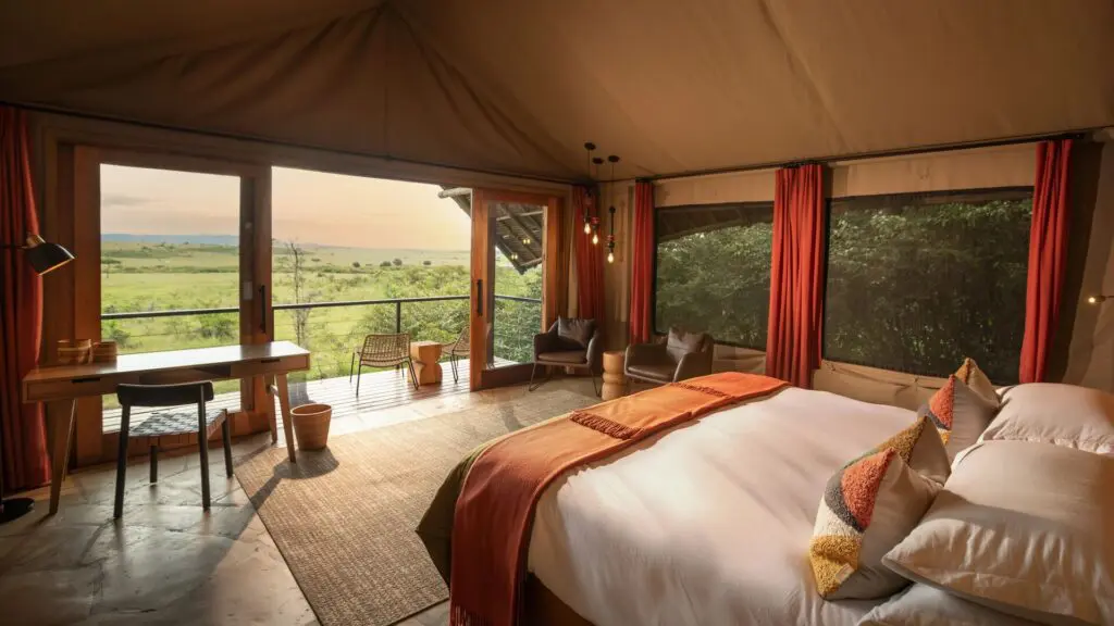 Interior of a luxury safari double room at Naboisho Camp with king bed, warm furnishings, large windows, and a private deck overlooking open savannah.