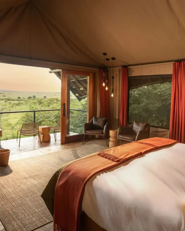 Interior of a luxury safari double room at Naboisho Camp with king bed, warm furnishings, large windows, and a private deck overlooking open savannah.