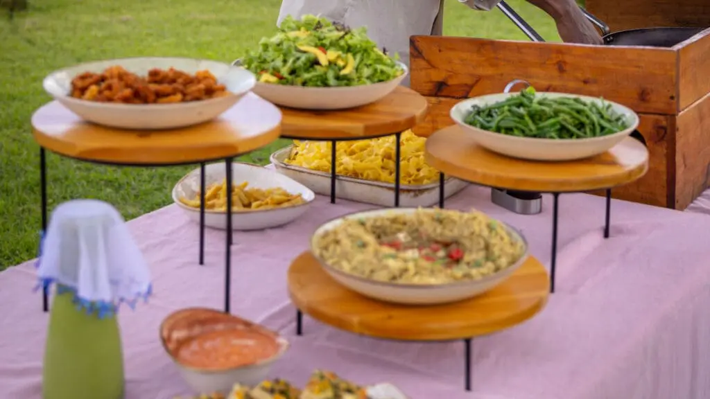 A selection of salads, vegetables, and pasta dishes arranged on a buffet table outdoors.