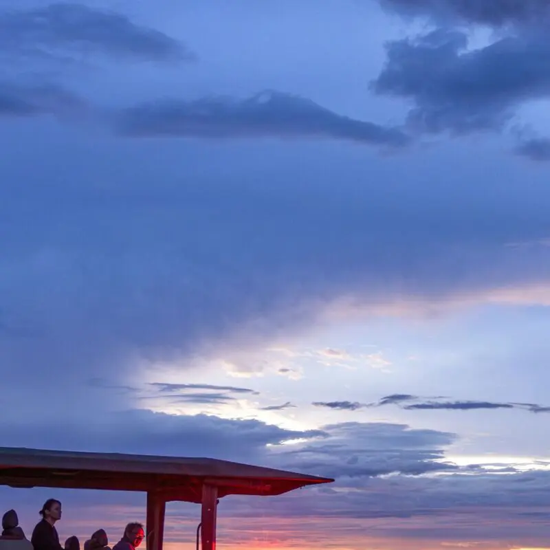 An open safari vehicle with guests overlooks the savannah on a night game drive at sunset under dramatic clouds