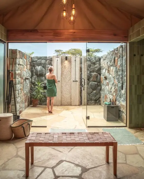 Naboisho's pen-air safari bathroom with stone walls, twin indoor wash areas, and a private outdoor shower courtyard.