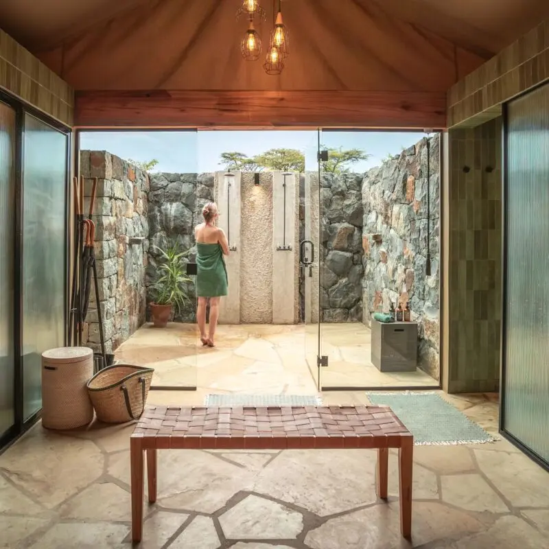 Naboisho's pen-air safari bathroom with stone walls, twin indoor wash areas, and a private outdoor shower courtyard.