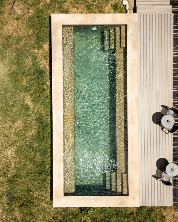 Overhead view of a private plunge pool at Namiri Retreats beside a wooden deck with chairs, set within grassy savannah and shaded by natural textures.