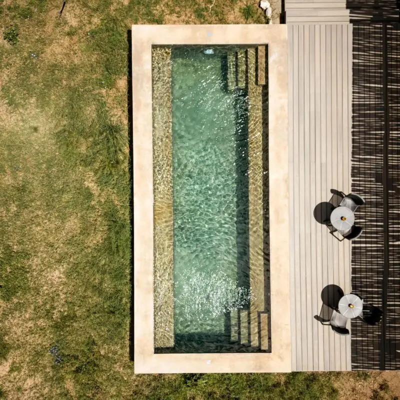Overhead view of a private plunge pool at Namiri Retreats beside a wooden deck with chairs, set within grassy savannah and shaded by natural textures.