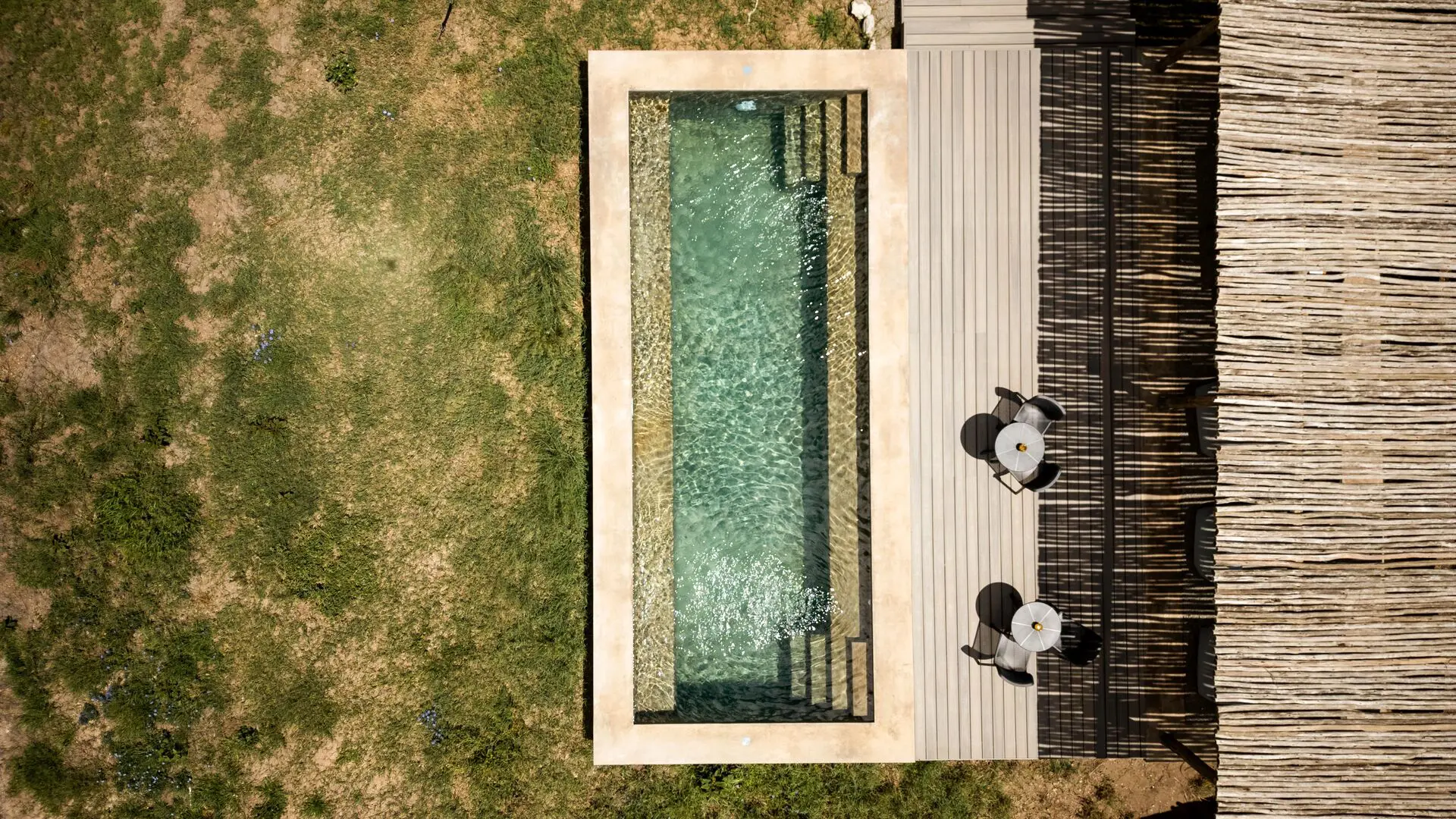 Overhead view of a private plunge pool at Namiri Retreats beside a wooden deck with chairs, set within grassy savannah and shaded by natural textures.