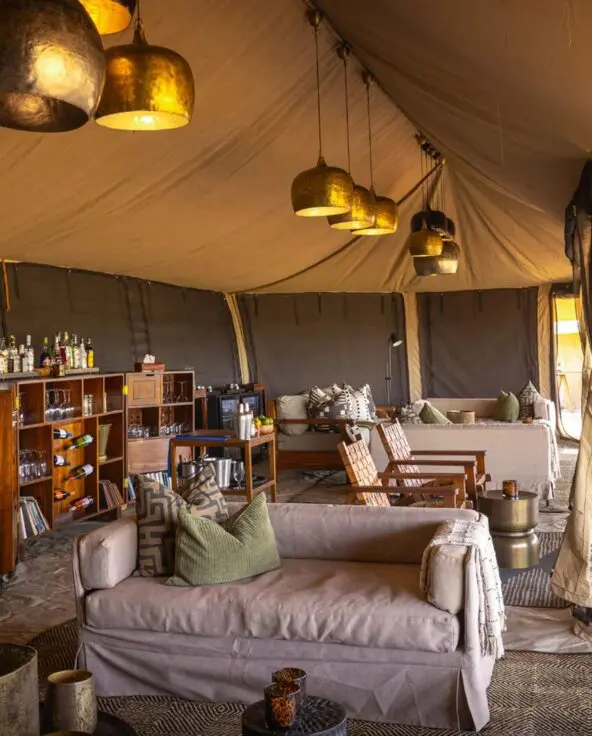 The interior of Olakira's lounge with comfortable seating, wooden bar shelves, hanging lantern lights, and open canvas walls leading to outdoor dining areas.