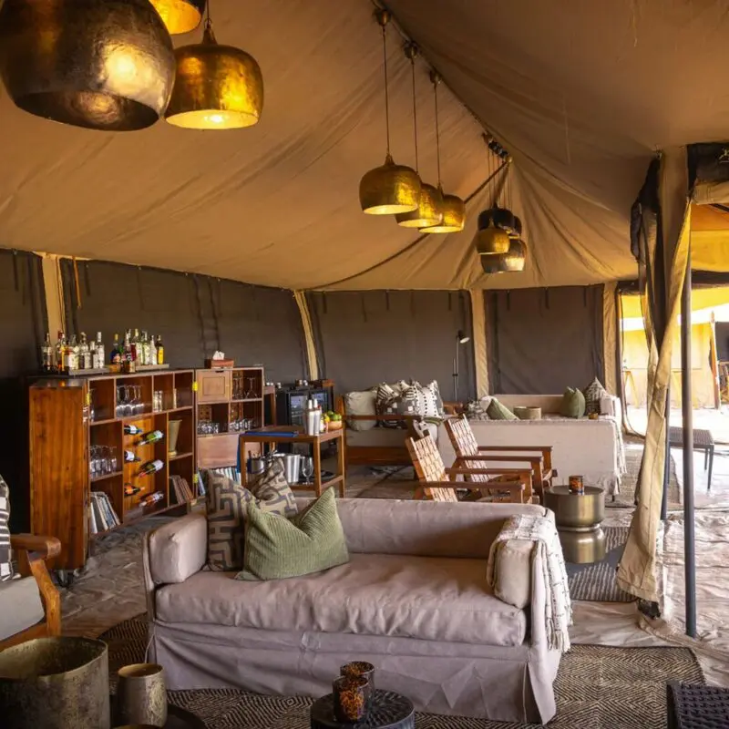 The interior of Olakira's lounge with comfortable seating, wooden bar shelves, hanging lantern lights, and open canvas walls leading to outdoor dining areas.