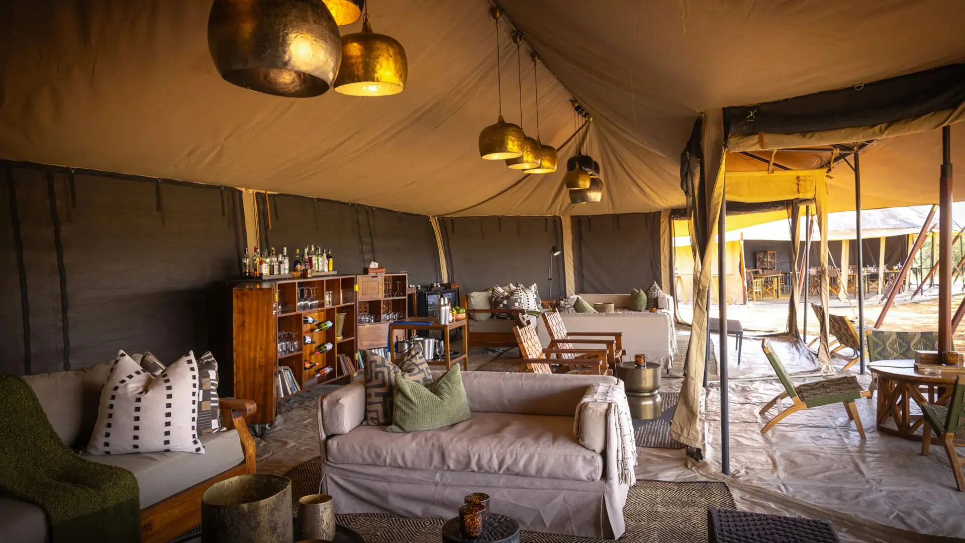 The interior of Olakira's lounge with comfortable seating, wooden bar shelves, hanging lantern lights, and open canvas walls leading to outdoor dining areas.