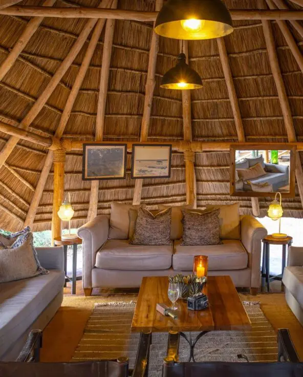 The interior of the circular thatched safari lounge at Oliver's Camp with comfortable sofas, soft lighting, wooden furniture, and a relaxed seating area designed for guests to unwind.