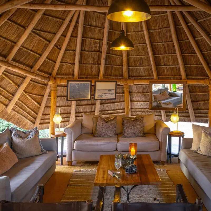 The interior of the circular thatched safari lounge at Oliver's Camp with comfortable sofas, soft lighting, wooden furniture, and a relaxed seating area designed for guests to unwind.