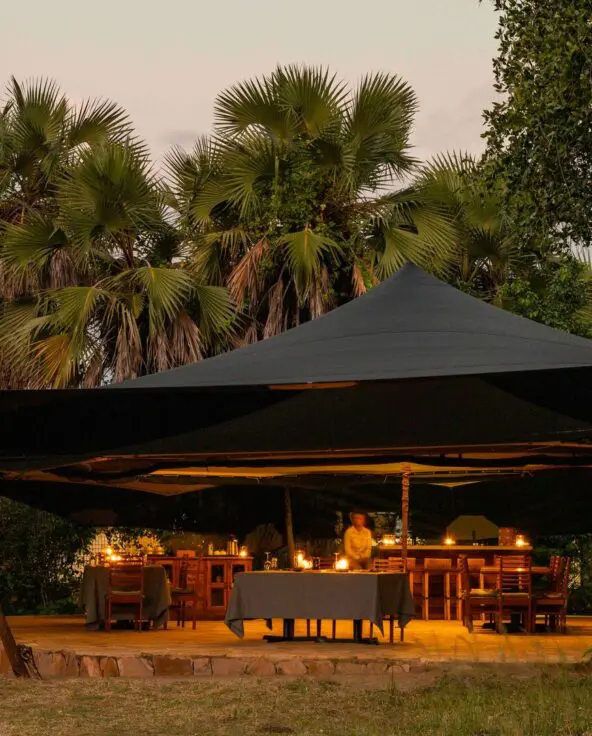 Roho ya Selous' open-air dining area under a canopy warmly lit with candles at dusk