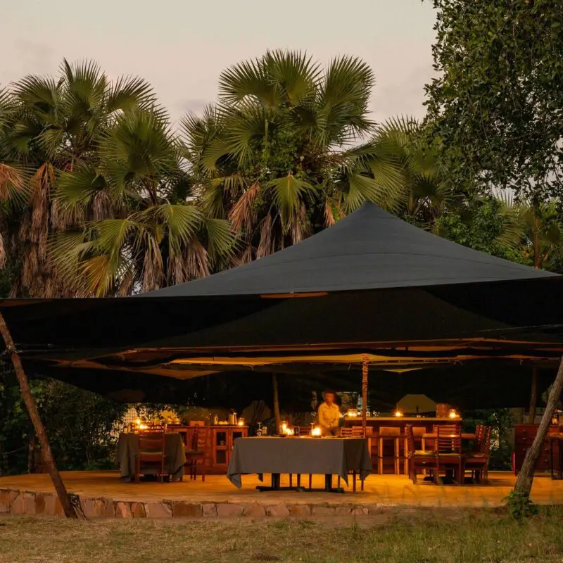 Roho ya Selous' open-air dining area under a canopy warmly lit with candles at dusk