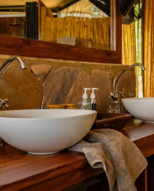 A guest bathroom at Roho ya Selous with double sinks, wooden counter, and bamboo walls
