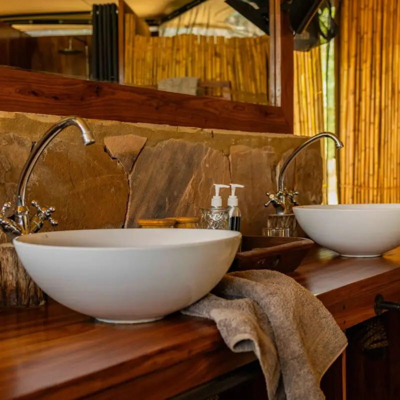 A guest bathroom at Roho ya Selous with double sinks, wooden counter, and bamboo walls