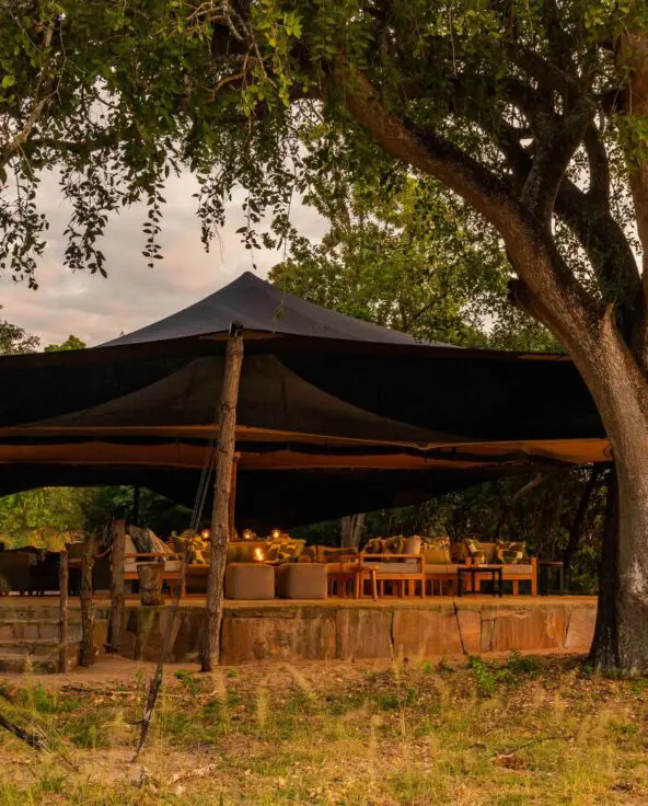 Roho ya Selous' lounge and dining area surrounded by trees and softly lit in the evening
