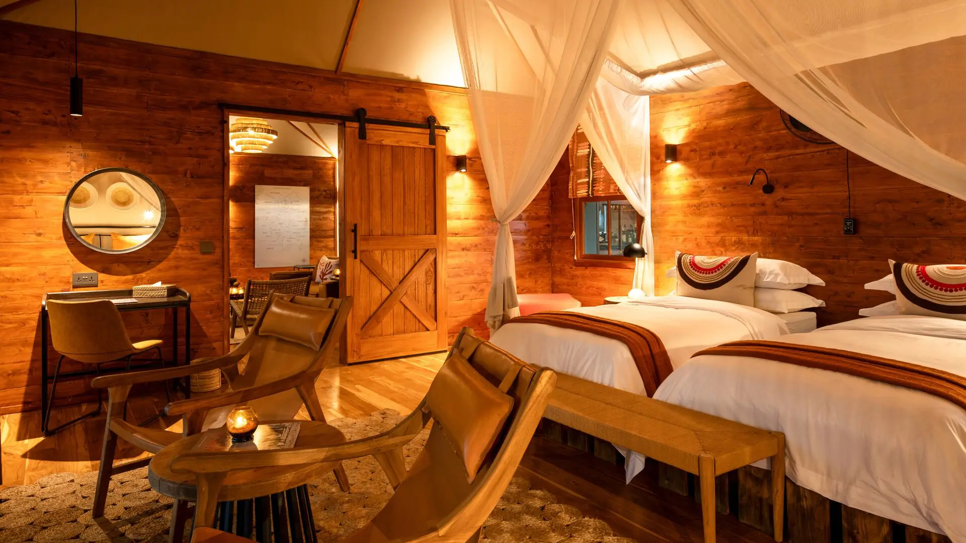 Interior of a twin bedroom at Sayari Retreat featuring two canopy beds with white linens, warm wooden walls, soft ambient lighting, leather lounge chairs, and a cosy, refined safari-lodge design.