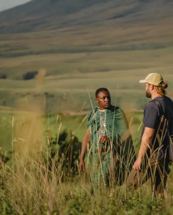 A guide and guest standing in tall grass discussing the landscape with rolling hills in the background