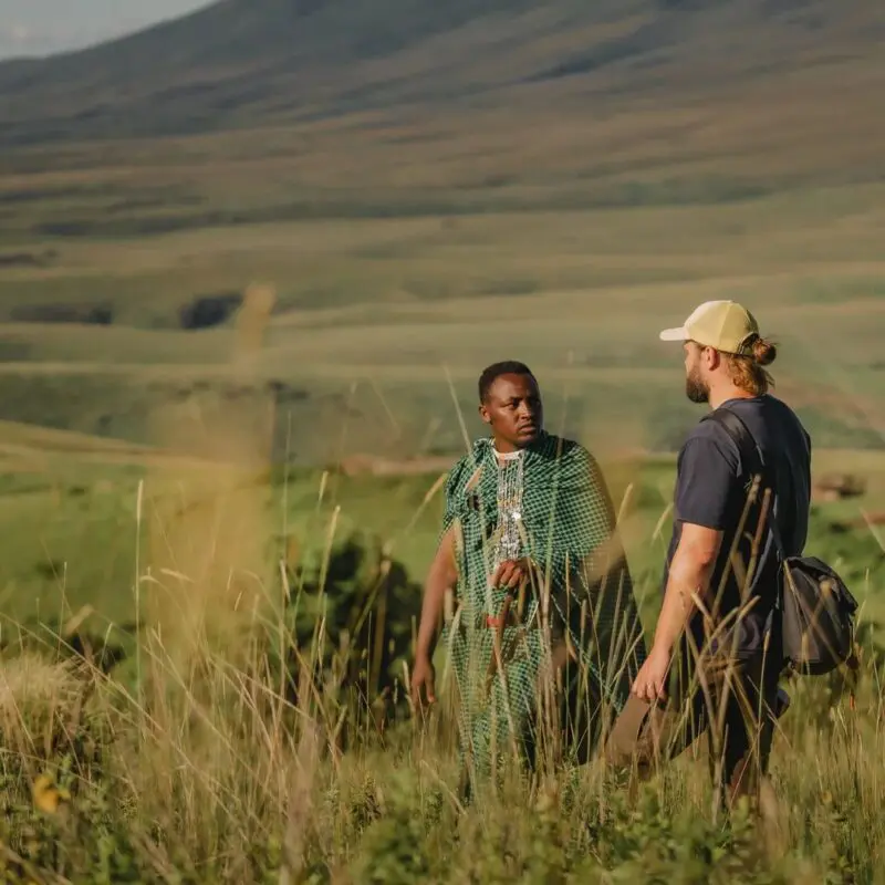 A guide and guest standing in tall grass discussing the landscape with rolling hills in the background