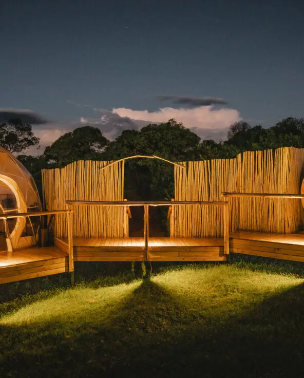 A lit spa area with dome structures and wooden decks surrounded by fencing at night