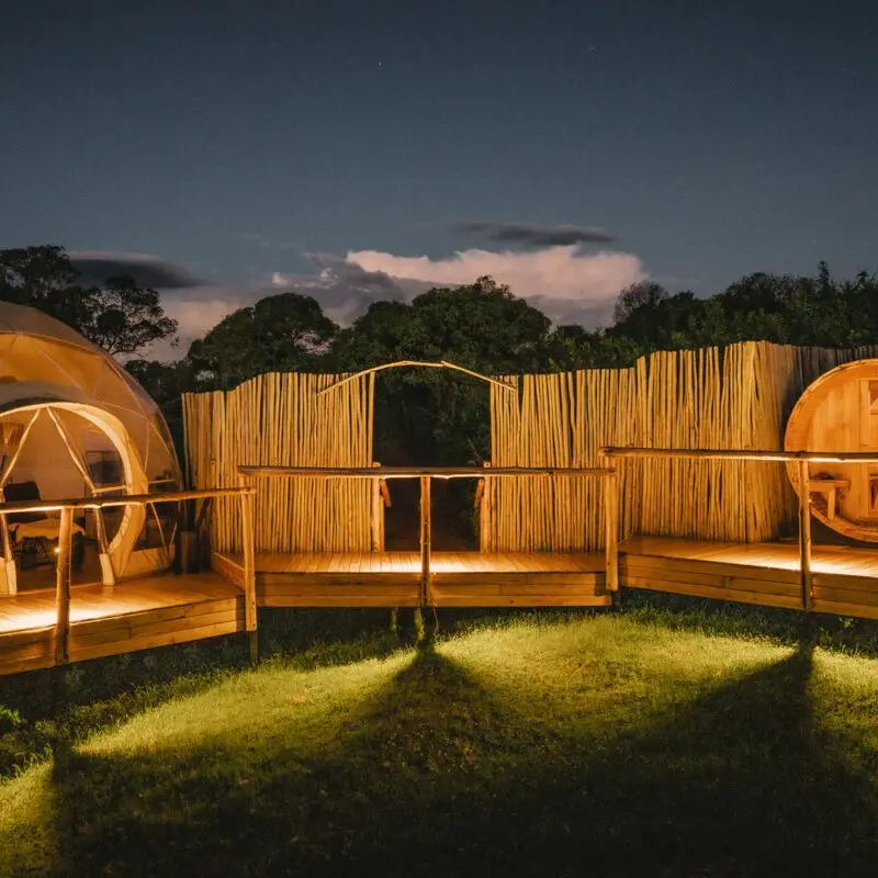 A lit spa area with dome structures and wooden decks surrounded by fencing at night