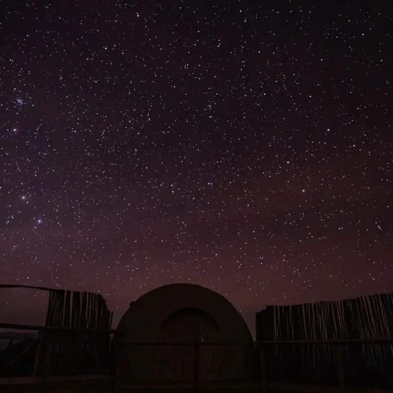 A silhouette of The Highlands Camp inn Africa against a dark starry sky.