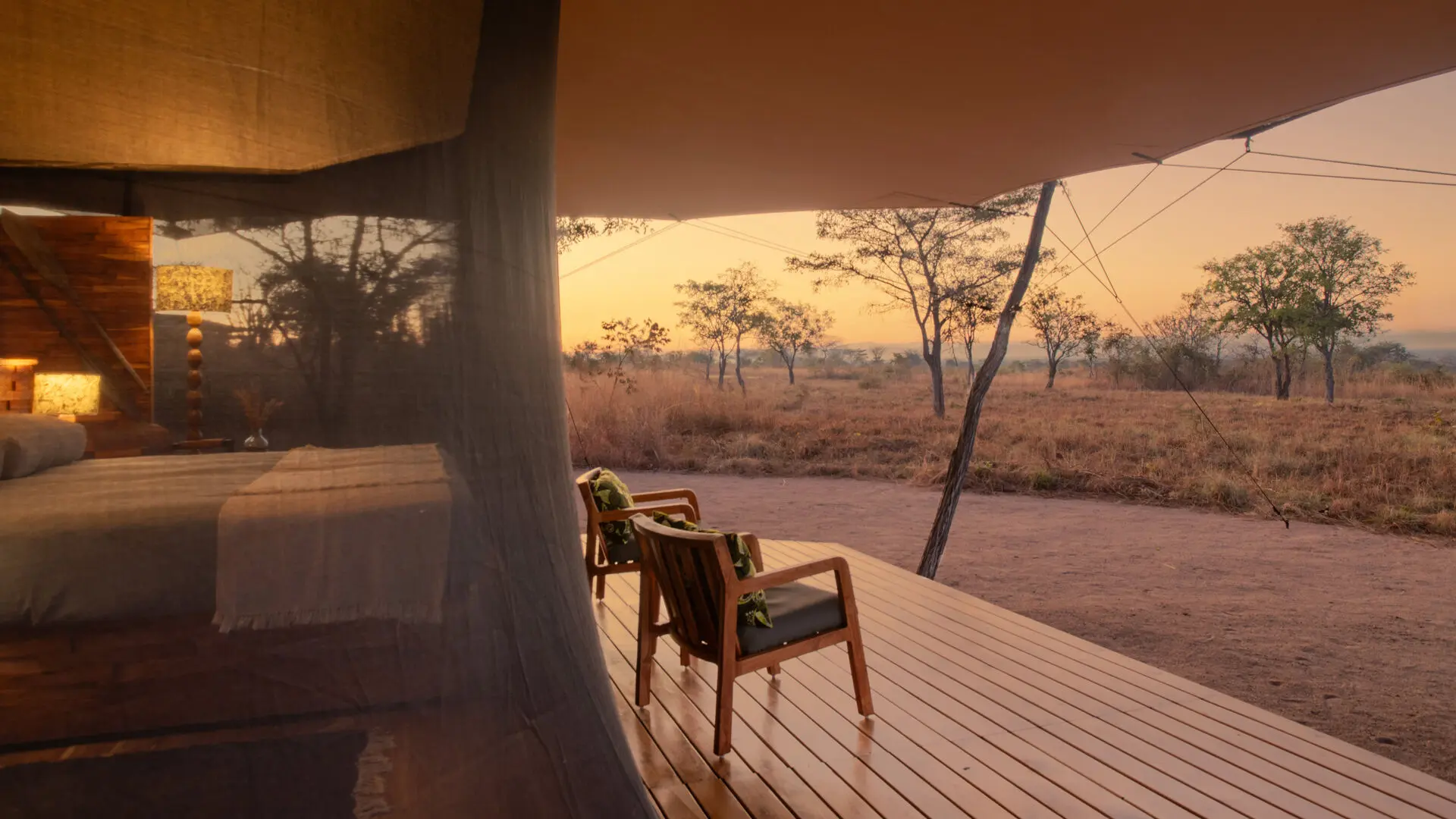 Two chairs on a wooden deck outside a guest room at Usangu Camp overlooking dry grassland at sunrise