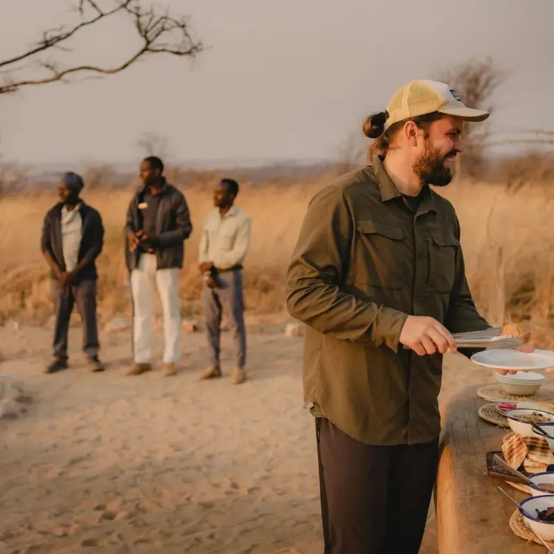An Asilia guest is served food from a bush breakfast with staff nearby