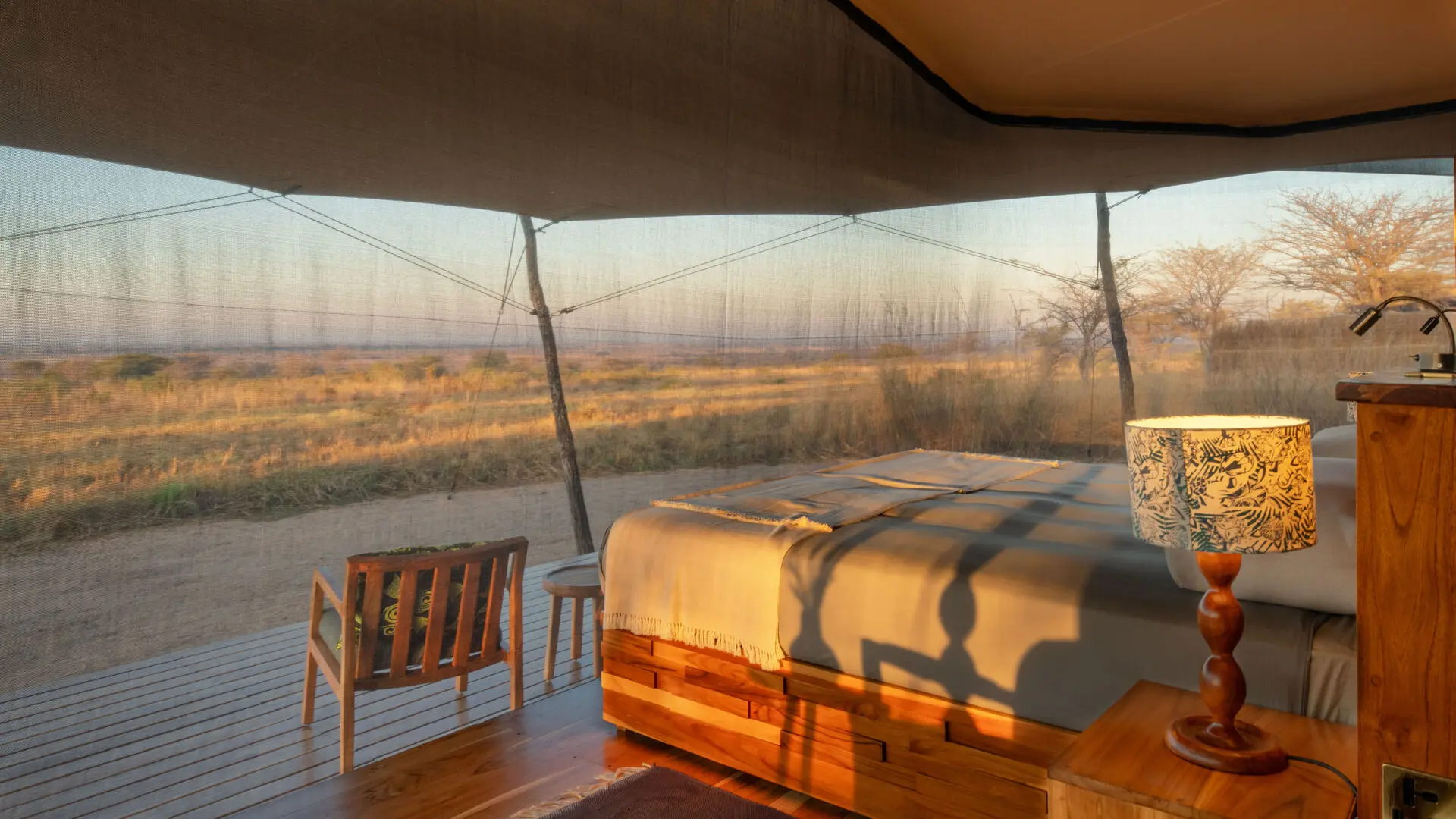 The interior of a guest bedroom at Usangu Camp with a bed facing expansive views of Ruaha National Park through mesh walls