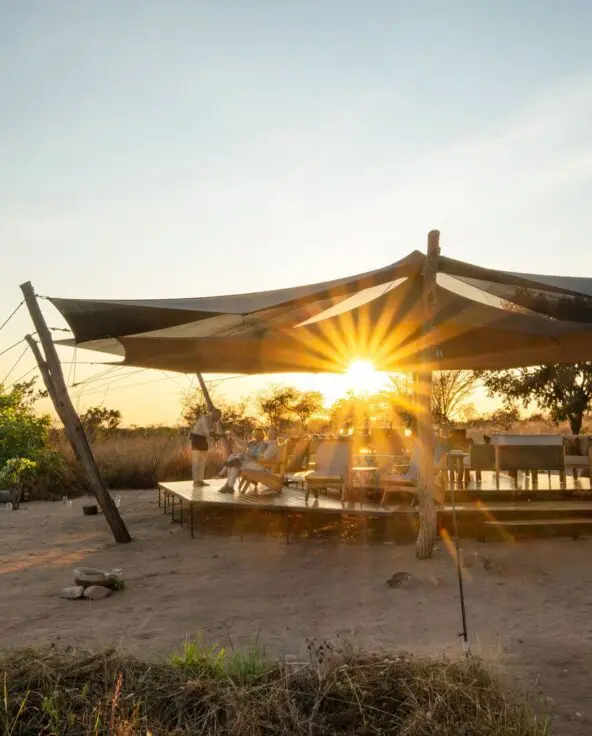 Usangu Camp's open-air lounge and dining area under canvas with guests enjoying the sunset light