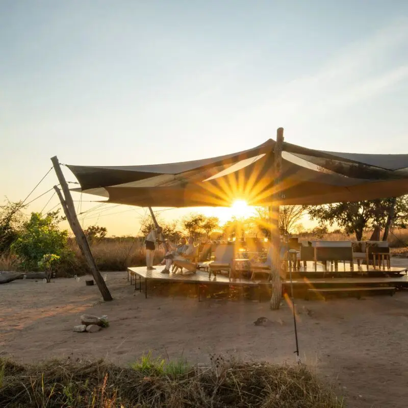 Usangu Camp's open-air lounge and dining area under canvas with guests enjoying the sunset light