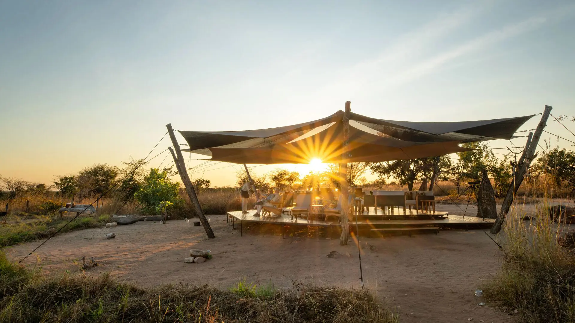 Usangu Camp's open-air lounge and dining area under canvas with guests enjoying the sunset light