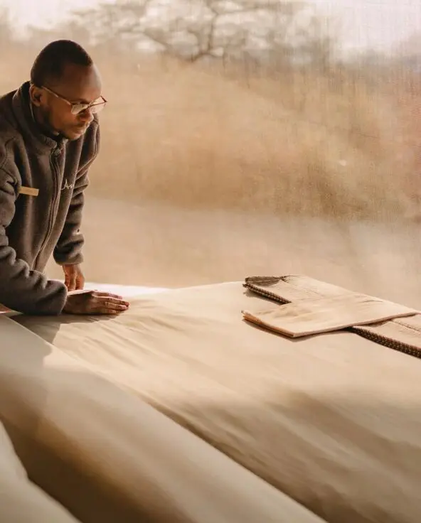 An Asilia staff member making a bed inside a safari tent at Usangu Camp with soft natural light filtering through mesh walls