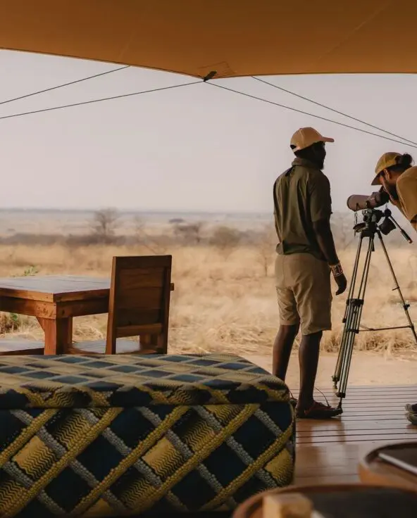 An Asilia guide and a guest using a telescope on a deck at Usangu Camp to observe the distant wildlife