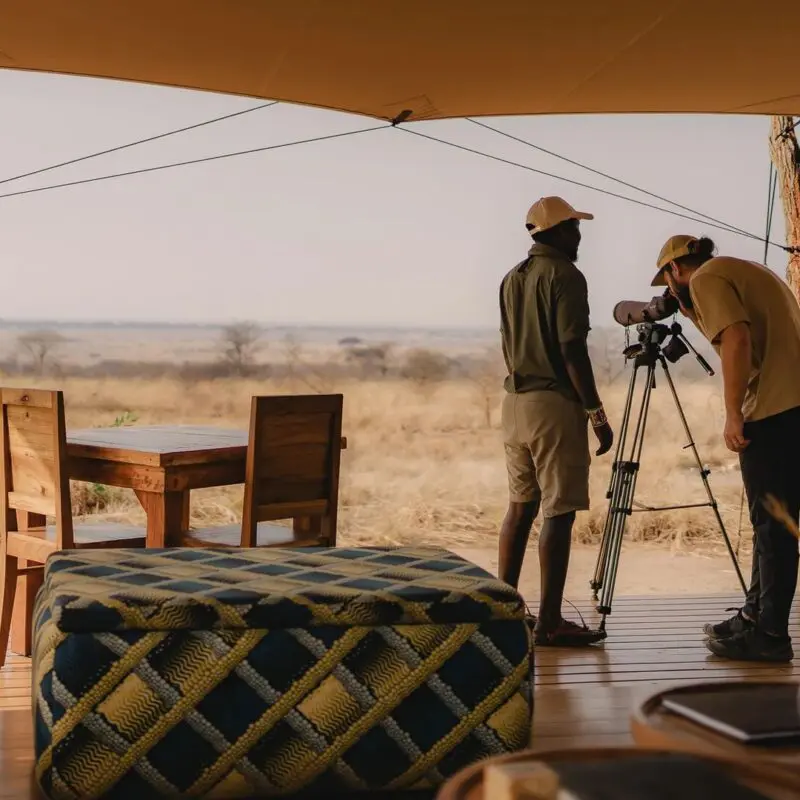 An Asilia guide and a guest using a telescope on a deck at Usangu Camp to observe the distant wildlife